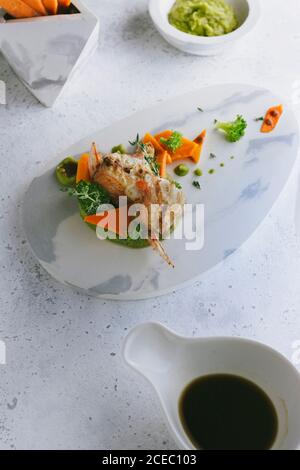 pesce scorpione alla griglia con purè di piselli e bastoncini di carote, su un piatto di marmo dall'alto Foto Stock