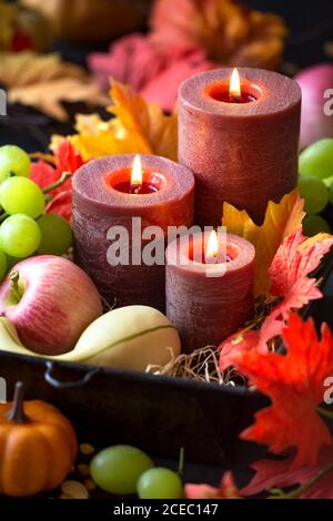 Composizione autunnale per il Ringraziamento con candele, foglie d'autunno, uva, zucche, semi di mais e coni di pino Foto Stock