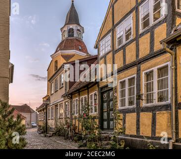 Alba al crepuscolo in un vecchio vicolo con case a graticcio, una torre della chiesa e ciottoli sui marciapiedi, Faaborg, Danimarca, 16 agosto 2020 Foto Stock