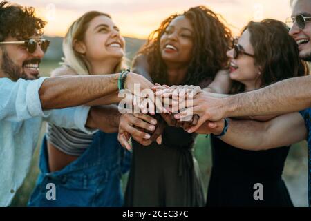 Gruppo di giovani che sorridono e tengono insieme le mani mentre si passa il tempo in natura Foto Stock