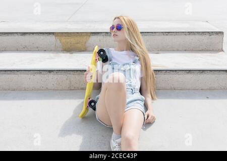 Bionda ragazza seduta sul pavimento con penny board Foto Stock