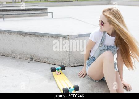 Bionda ragazza seduta sul pavimento con penny board Foto Stock