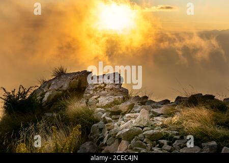 Cima della montagna coperta di vegetazione autunnale e illuminata dai raggi del sole che tramonta attraverso le nuvole. Belluno, Italia Foto Stock