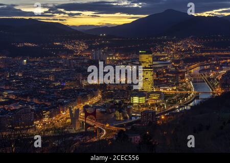 BILBAO, SPAGNA - 23 GENNAIO 2019: Vista panoramica della città moderna situata sul fiume tra le pittoresche montagne al crepuscolo Foto Stock