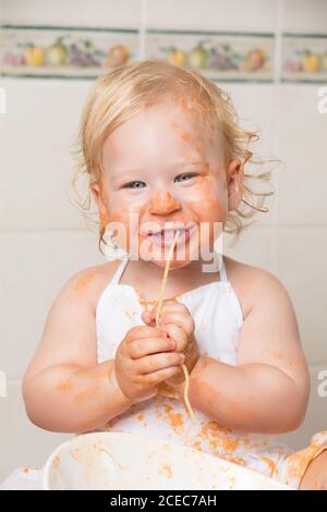 Bambino allegro seduto su una favola e divertendosi mentre si mangia la pasta dalla ciotola. Foto Stock