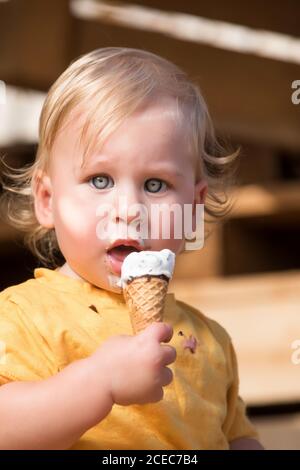 Ragazzo in abiti gialli mangiando gelato al cioccolato con cono di waffle. Foto Stock