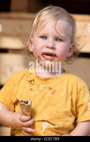 Ragazzo in abiti gialli mangiando gelato al cioccolato con cono di waffle. Foto Stock