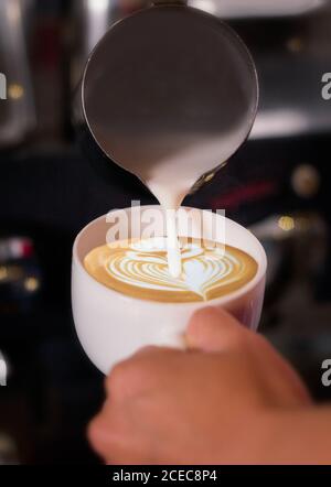 Crop mano di irriconoscibile barman versando crema al latte e disegnare un fiore. Foto Stock