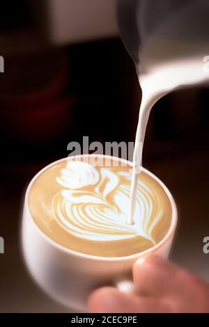 Crop mano di irriconoscibile barman versando crema al latte e disegnare un fiore. Foto Stock