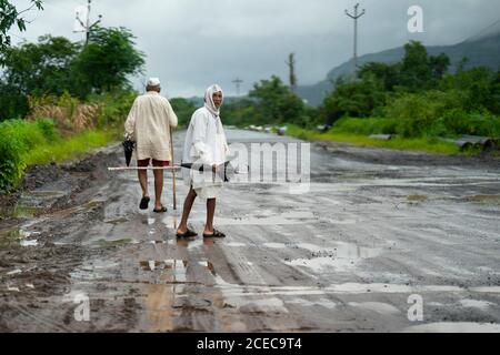 abitanti del villaggio di maharashtria che camminano con ombrelloni in una giornata piovosa indossare dhoti Foto Stock