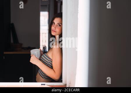 Giovane donna bere caffè vicino alla finestra Foto Stock