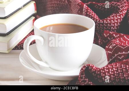 Una tazza di caffè, una sciarpa calda e libri si trovano su uno sfondo bianco boscoso Foto Stock