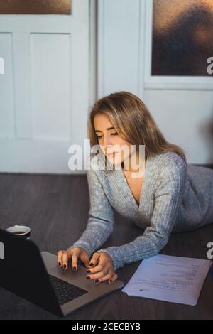 Donna sdraiata sul pavimento che lavora con un computer portatile Foto Stock