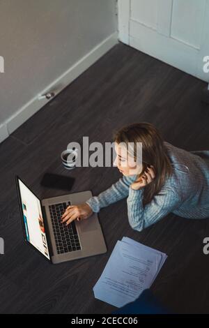 Donna sdraiata sul pavimento che lavora con un computer portatile Foto Stock