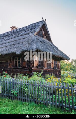 Piccola recinzione che racchiude vecchia capanna di legno e giardino con grazioso fiori contro il cielo blu in splendida campagna Foto Stock
