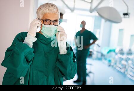 Ritratto di chirurgo femminile che indossa una maschera chirurgica durante l'intervento camera Foto Stock