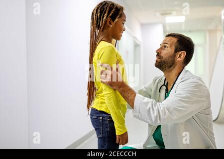 Dottore che ha conversazione con piccola ragazza triste all'ospedale. Dottore consolante bambino Foto Stock