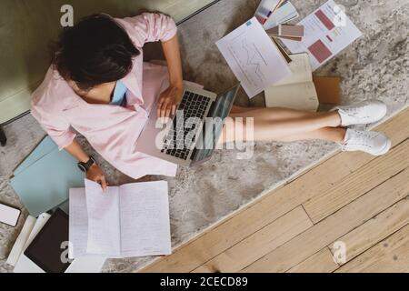 Vista dall'alto di una giovane donna d'affari seduto sul pavimento che lavora con documenti e che scrive sul laptop. Foto Stock