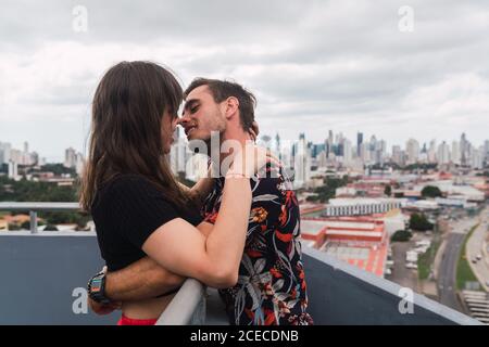 Giovane coppia baciandosi su un balcone e godendosi la vista di una città moderna Foto Stock