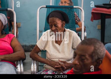 LA HABANA, CUBA - 6 NOVEMBRE 2018: Anziana donna afroamericana seduta sulla sedia del campo tra le persone di raccolto in stanza a Cuba Foto Stock