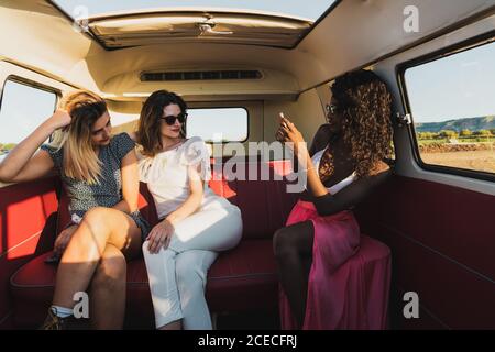 Tre allegre giovani donne sedute all'interno di un furgone d'epoca e in posa per selfie mentre si viaggia insieme Foto Stock