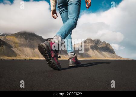 Foto senza volto dal basso di Donna in scarpe da trekking a piedi sul terreno della valle con montagne sullo sfondo, Islanda. Foto Stock