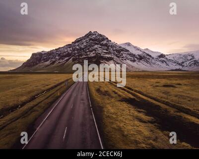 Strada asfaltata in Islanda attraverso ampio spazio aperto con nuvole e le montagne Foto Stock