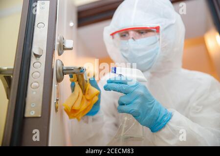 Disinfezione e pulizia delle maniglie della porta della casa da infezioni da virus e microbi in tuta biochimica. Concetto di protezione del coronavirus Foto Stock