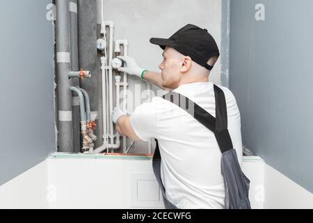 Idraulico maschio controlla i tubi per l'approvvigionamento centrale di acqua calda e fredda dell'appartamento Foto Stock