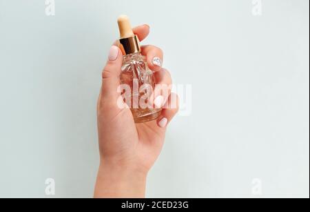 Vista dall'alto di una donna anonima con mani curate che mostrano un vuoto bottiglia di olio essenziale su fondo azzurro Foto Stock