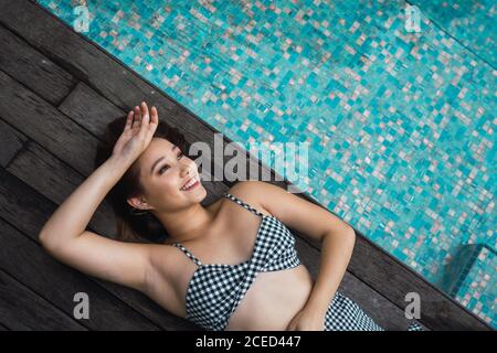 Dall'alto sorridente bella donna asiatica sdraiata e rilassante in piscina. Foto Stock