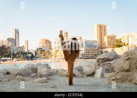 Donna in generale elegante divertirsi e fare split mentre in piedi tra le rocce sulla riva con il paesaggio urbano sullo sfondo Foto Stock