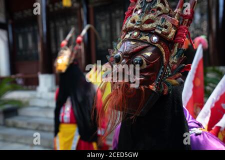 Gruppo di donne Miao di minoranza etnica in costumi tradizionali luminosi e maschere in piedi con l'uomo in costume giallo all'aperto a. Muro di un edificio cinese a Guizhou Foto Stock