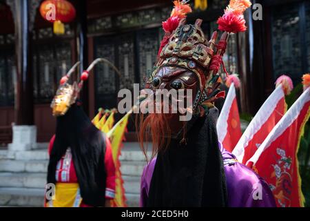 Gruppo di donne Miao di minoranza etnica in costumi tradizionali luminosi e maschere in piedi con l'uomo in costume giallo all'aperto a. Muro di un edificio cinese a Guizhou Foto Stock