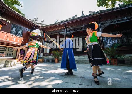 GUINZHOU, CINA - 14 GIUGNO 2018: Uomo del gruppo etnico Miao in abiti blu che suonano strumenti musicali tradizionali e donne in brillanti costumi locali che ballano intorno a lui durante il festival nel villaggio nella provincia di Guizhou in Cina Foto Stock