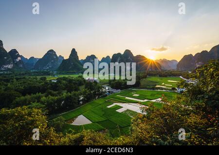 Vista aerea della pittoresca zona bassa di risaie con piccolo Case circondate da montagne nella provincia cinese di Guangxi Foto Stock