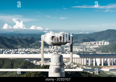 Costruzione bianca di moneta binoculare spettatore sulla terrazza contro il paesaggio urbano nelle montagne tropicali, Phoenix Park, Cina Foto Stock