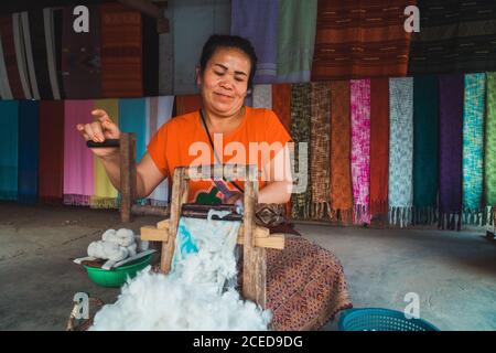 Donna asiatica allegra adulta seduta nel negozio e lavorando con tessuto. Foto Stock