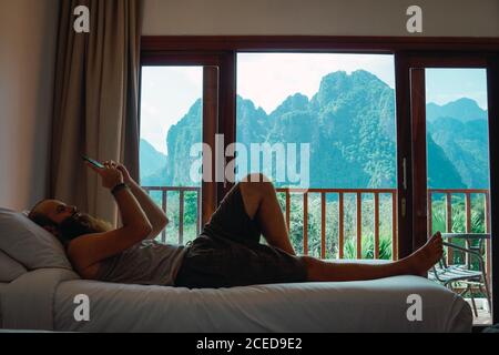 uomo che si rilassa a letto con smartphone a casa Foto Stock