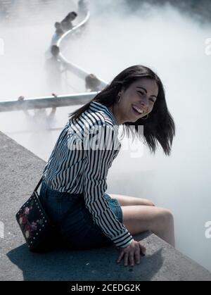 Ridendo ragazza sulla recinzione in nebbia d'acqua Foto Stock