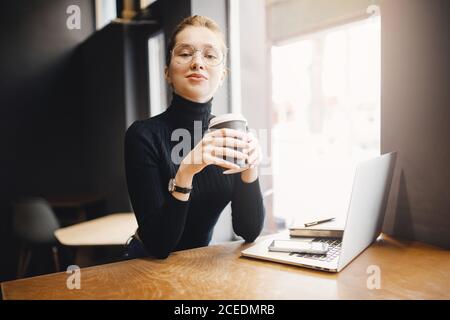 Giovane donna d'affari che lavora con un computer portatile e beve caffè. Informazioni sulla ricerca dei processi di quarantena Foto Stock
