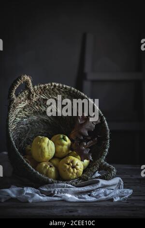 Cestino rustico con foglie secche d'autunno e frutta fresca matura†mentendo vicino al tovagliolo sul piano portapaziente in legno Foto Stock