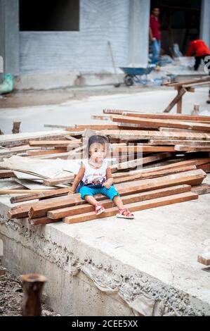 Una bambina tailandese carina si siede tra le macerie di un cantiere a Bangkok Thailandia. Foto Stock