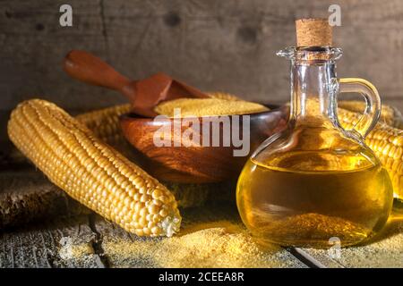 Granoturco grits polenta e olio di mais in una bottiglia, semole di mais, e corncobs su una tavola rustica di legno. Il concetto di alimentazione sana e nutrizione. Foto Stock