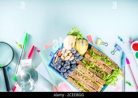 Pranzo sano scuola per bambini: Sandwich, verdure, frutta e bottiglia di acqua minerale, con forniture scolastiche su, su sfondo azzurro spazio copia Foto Stock