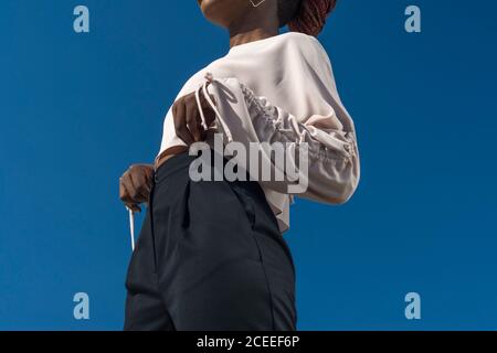 Primo piano ritratto di ragazza nera alla moda, ragazza africana in blusa e pantaloni da lavoro, in posa. Sullo sfondo del cielo blu. Alla moda Foto Stock