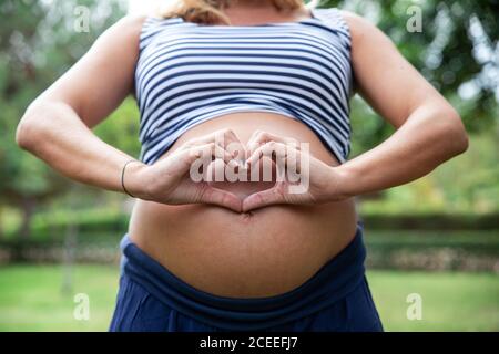 Sorridente incinta attraente Donna che mostra il simbolo del cuore Foto Stock