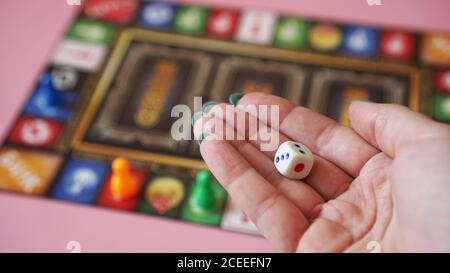 La mano getta i dadi sullo sfondo di colorati giochi da tavolo sfocati, momenti di gioco Foto Stock