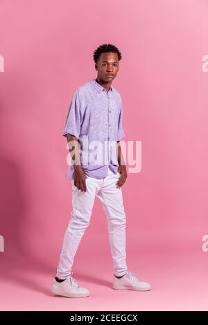 Elegante giovane uomo allegro che posa su sfondo rosa Foto Stock