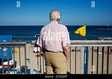 BARCELLONA - 10 luglio 2011: Vista posteriore dell'uomo anziano in piedi vicino recinzione metallica e guardando la spiaggia sullo sfondo del mare. Foto Stock